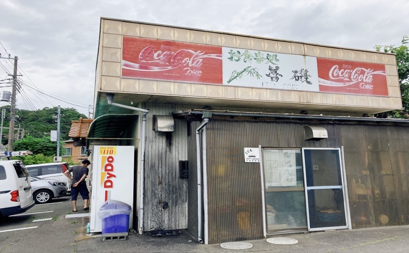 お店の看板とコカコーラ自販機がある建物の写真