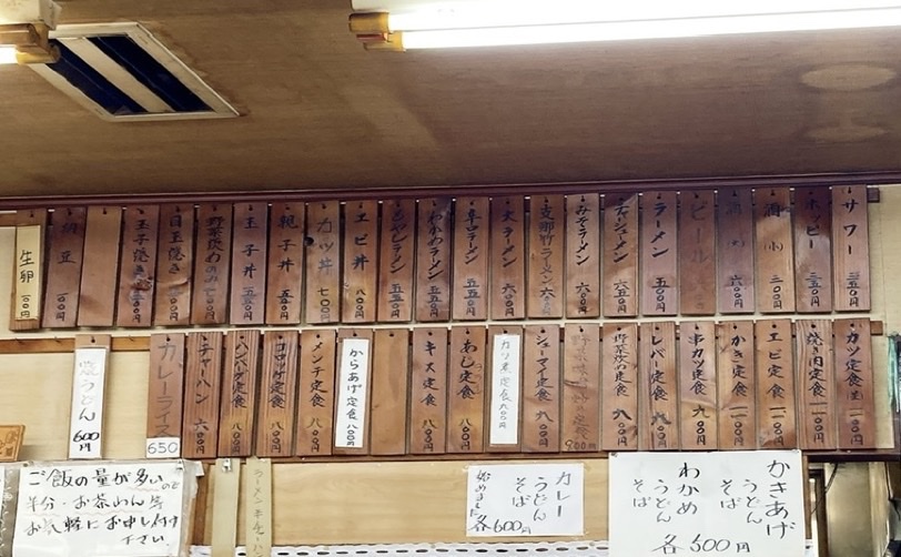 壁に掛けられた料理のメニュー。様々な料理名と価格が書かれている。
