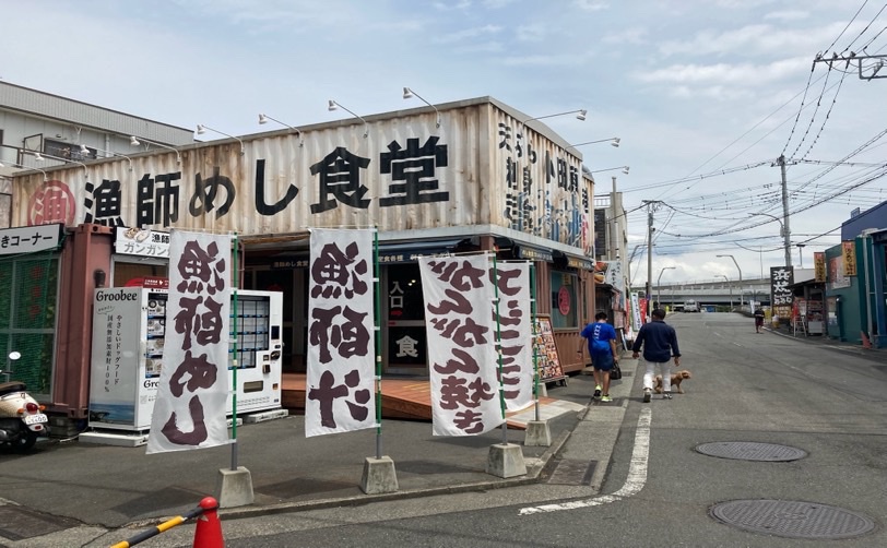 コンテナを利用した漁師めし食堂の外観 旗には魚稲などと書かれている 犬の散歩をする男性達