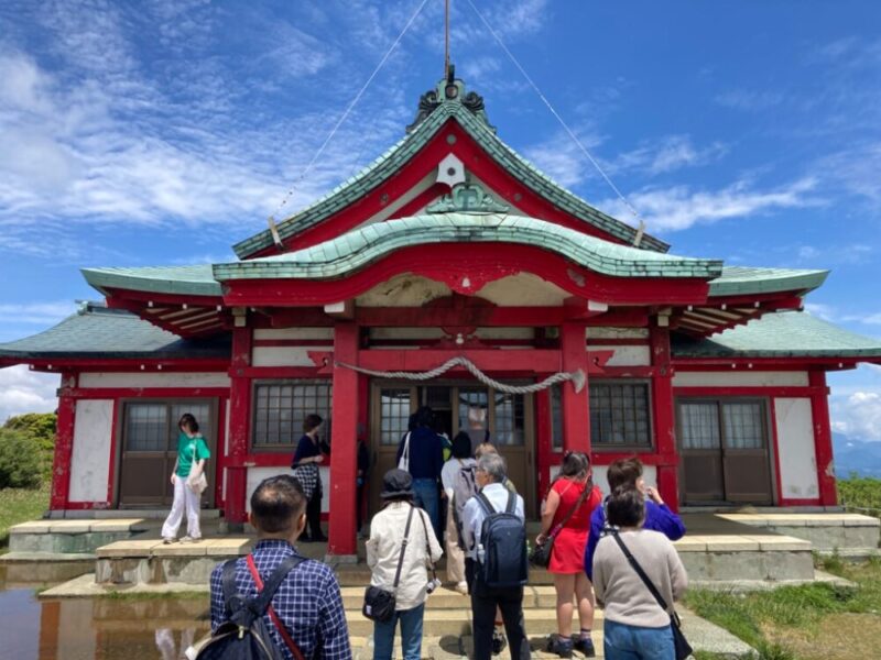 青空の下、朱色と緑の屋根の神社を訪れる人々