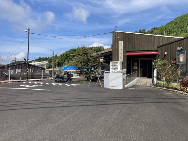 黒いスクーターが駐車場のそばに止まっているまばゆい日差しの下、木造の建物の入り口で