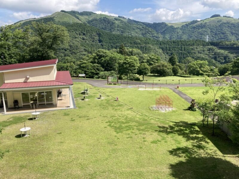 緑の芝生と赤い屋根の建物 奥に山が広がる景色
