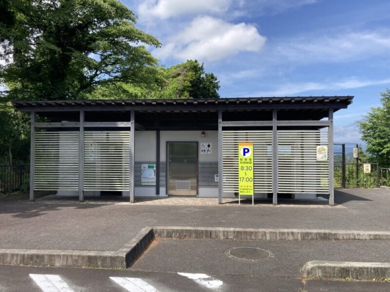 公衆トイレの建物と駐車場利用時間の看板 青空と木々