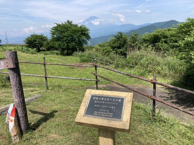 山の上の広場に立つ標識と柵、そして遠くに富士山が見える景色