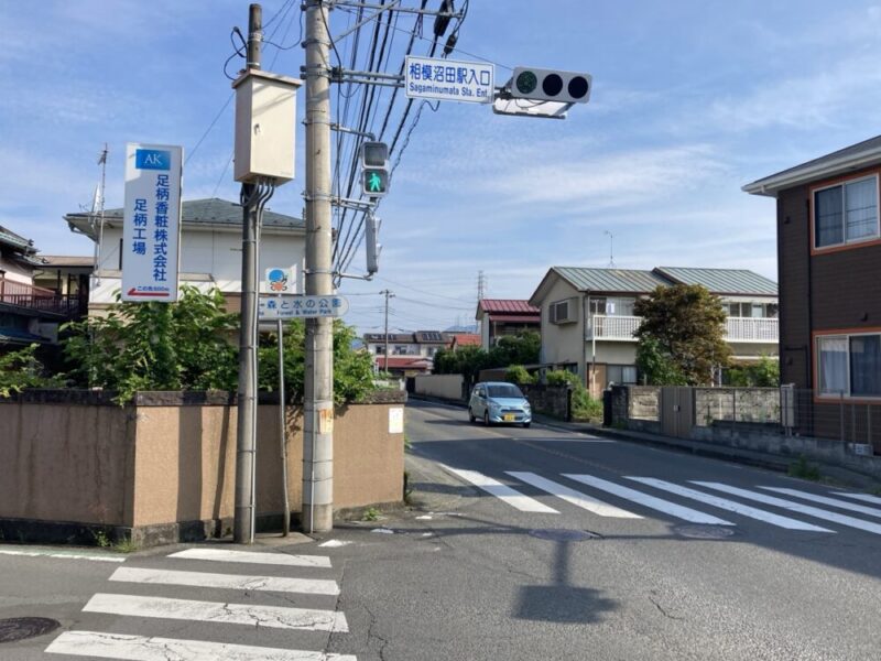 小田急線 相模大野駅入口前の交差点と、足立工場を示す看板と青い空。
