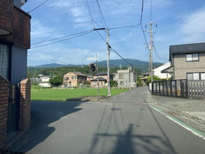 田んぼの横の道を、家と山々が見える風景