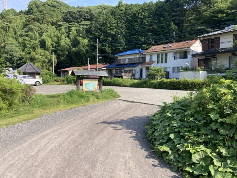 駐車場から見たのどかな村の風景、山には緑が生い茂り、小さな家が建ち並び、案内板が立てられている