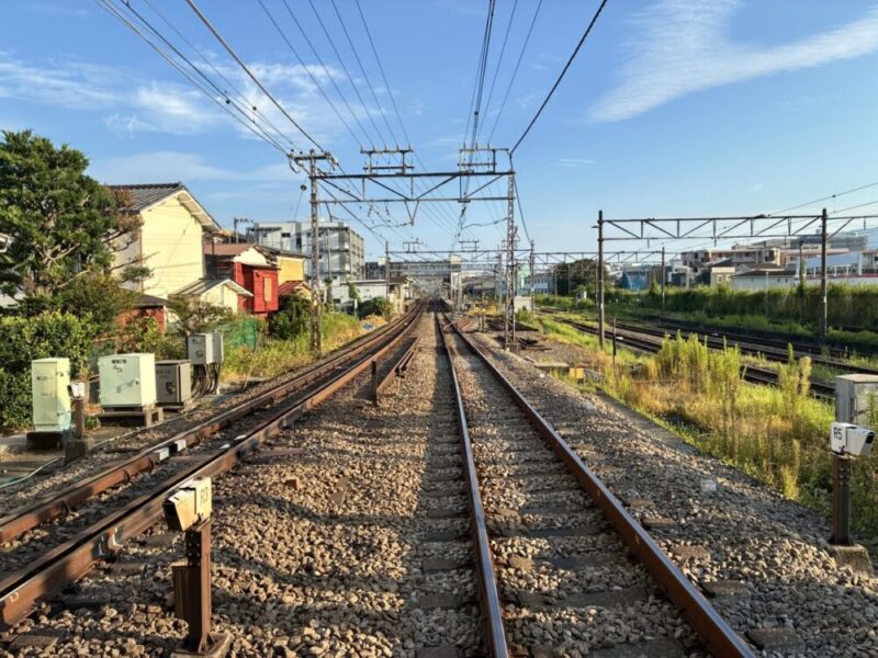 青空の下、住宅街をまっすぐ遠くへ伸びる複数の鉄道線路