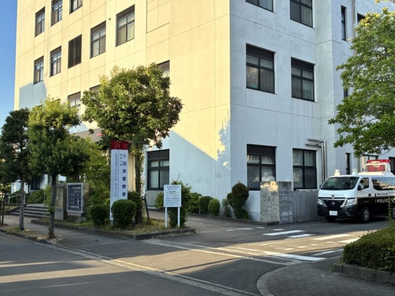 小田原警察署の白い建物入口の赤い看板と警察のパトカー