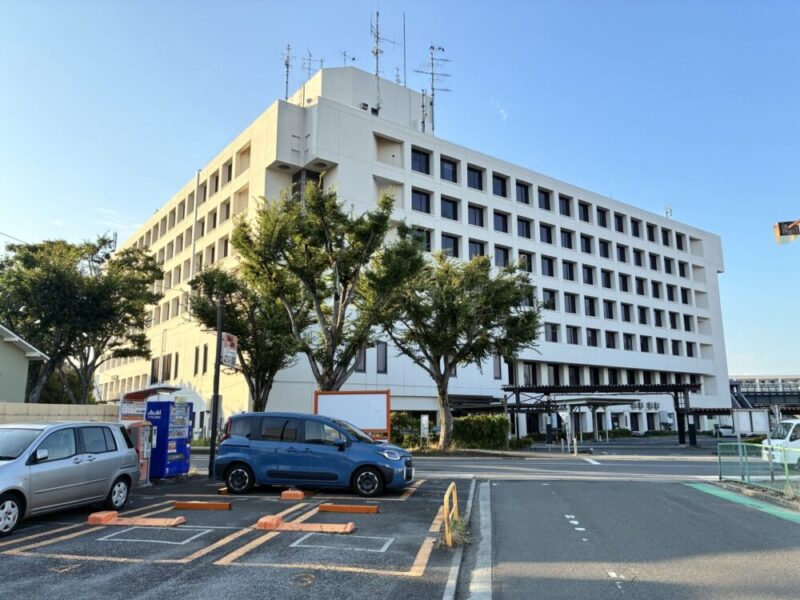 青空の下、駐車場に車が停まる大きな白い建物