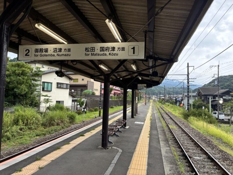 日本の駅ホームに2本の線路が遠くまで伸びるホームには屋根とベンチがあり御殿場沼津方面と松田国府津方面を示す看板が見える