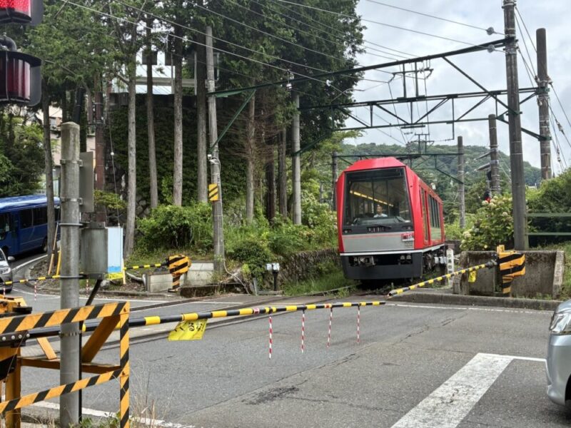 赤い電車が遮断機のある踏切に停車している様子