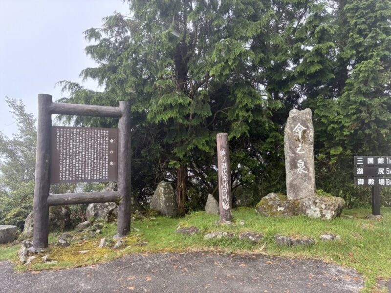 木々に囲まれた山道にある命之泉と書かれた石碑 場所の解説板 三国峠や湖尻への距離を示す案内標識