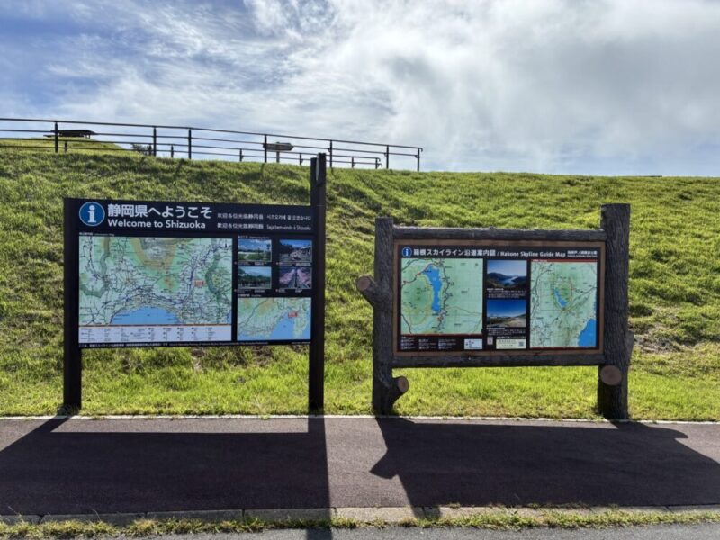 静岡県へようこそと書かれた看板と箱根スカイラインの案内板が芝生の斜面に並ぶ屋外の風景
