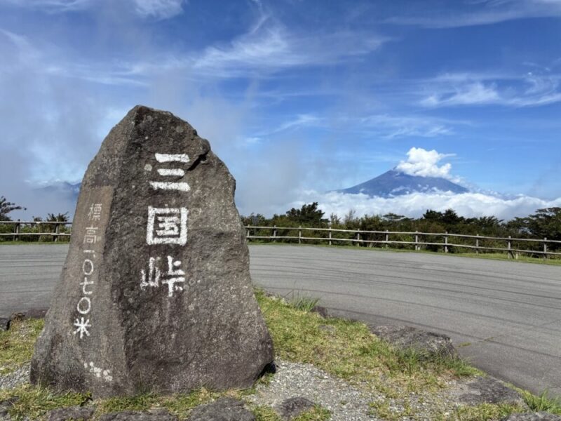 三国峠の標高を示す石碑と雲に覆われた富士山が青空の下に広がる景色