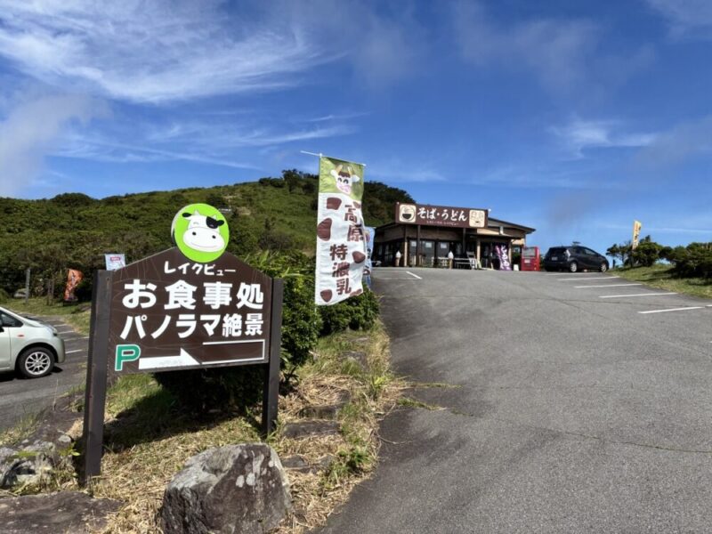青空の下 緑の丘にあるレイクビューお食事処パノラマ絶景の看板と高原の駐車場 そばうどん店