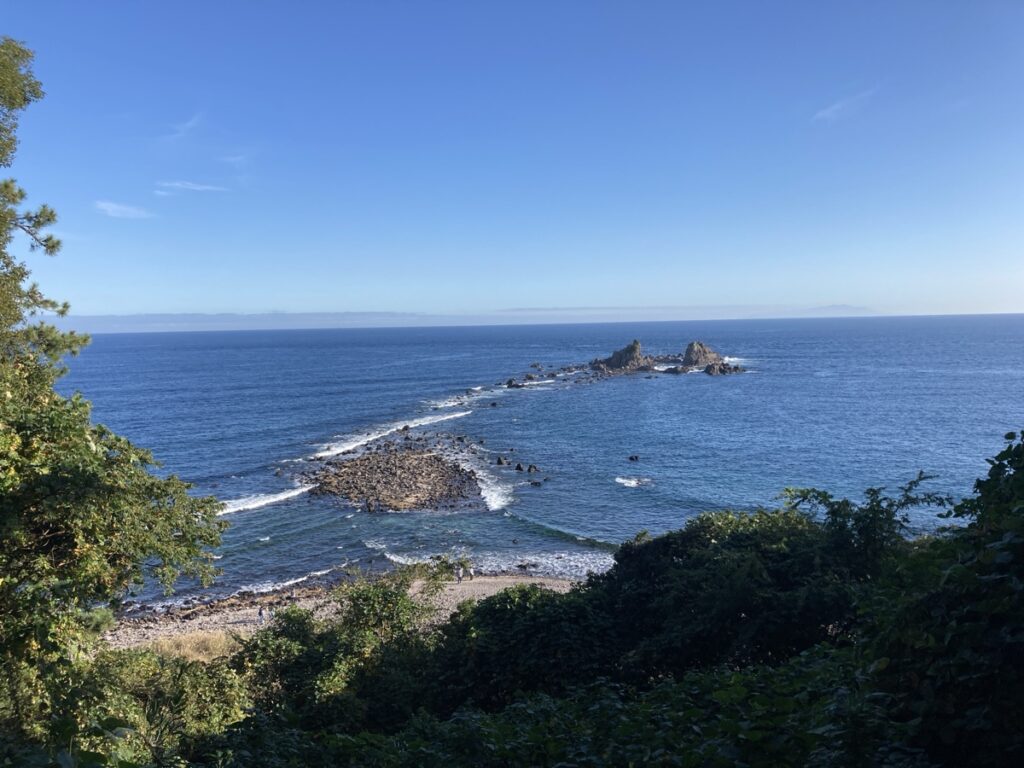 緑の木々越しに見る青い海と空 浅瀬の岩の道が沖の小島へ連なる