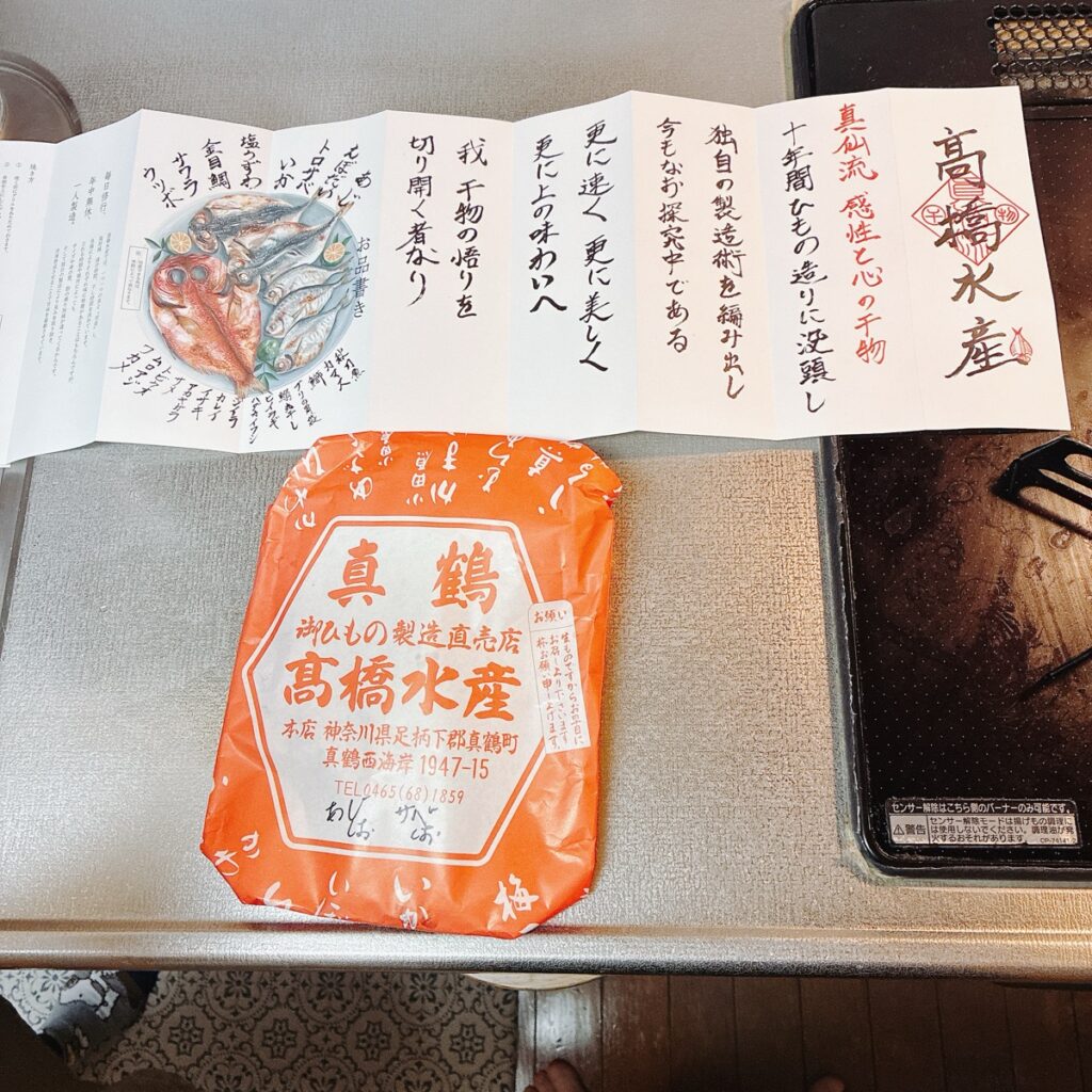 真鶴の高橋水産が販売する干物の赤い包みと複数の魚の種類が描かれた案内文