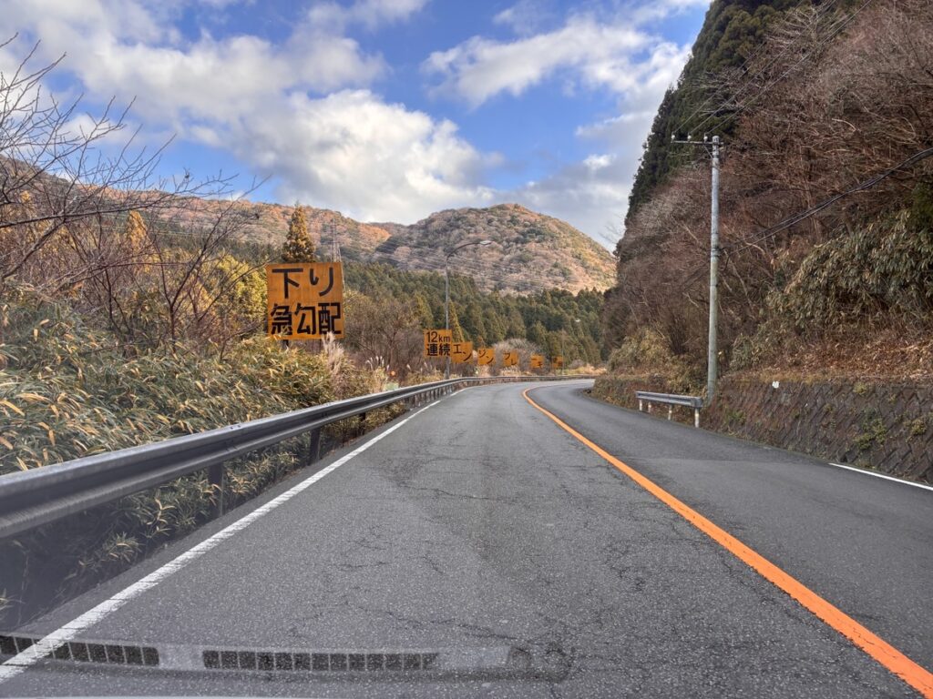 下り急勾配の標識が立つ冬枯れの山道のカーブ