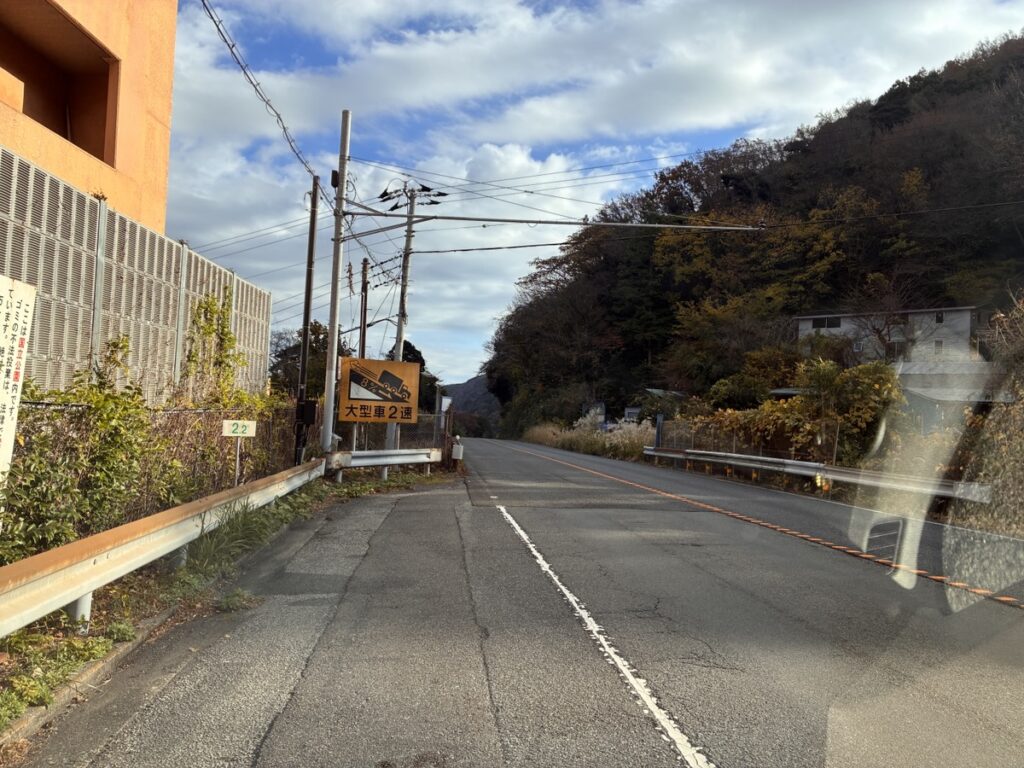 オレンジ色の建物と山の間の道路 大型車2週の標識