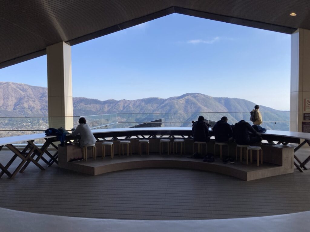 山並みを望む展望台で人々がカウンターに座って景色を見ている