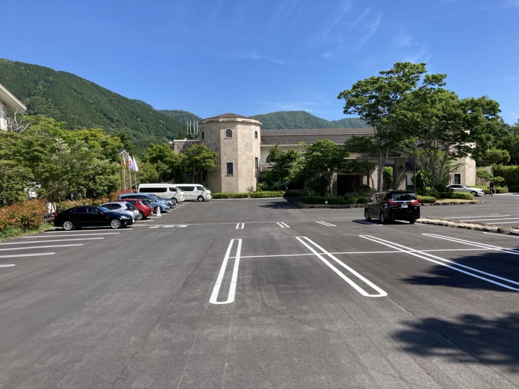 晴れた日に緑の山を背景にした丸い塔のある石造りの建物と広い駐車場