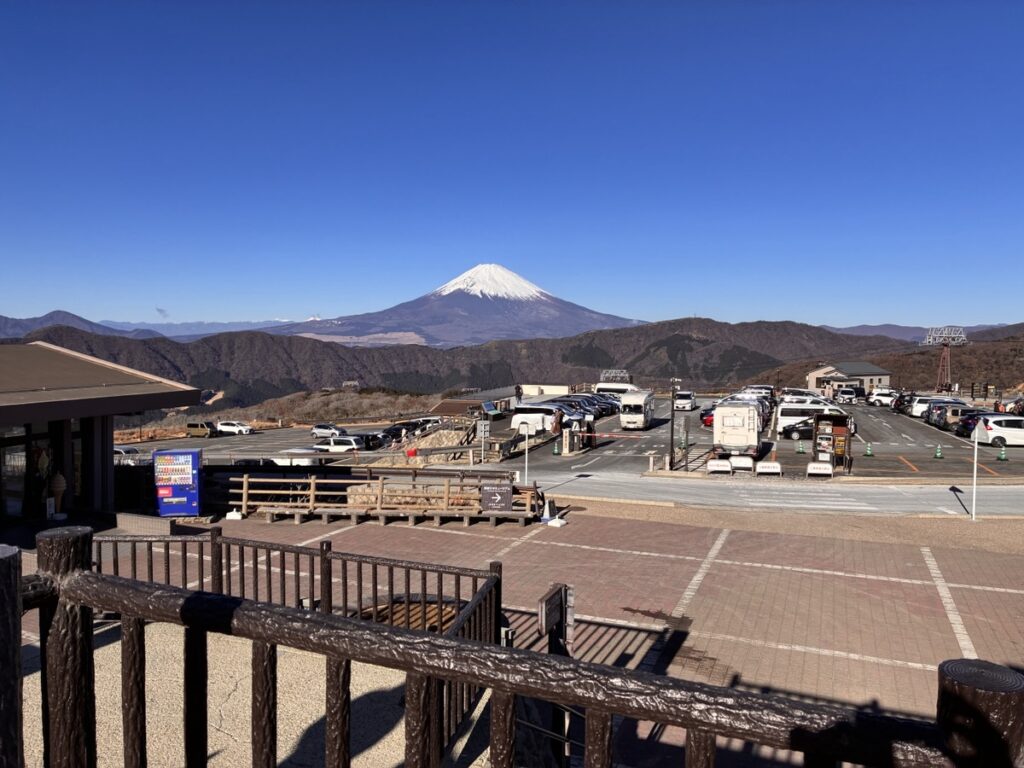 青空の下 雪化粧した富士山と多くの車が停まる展望台の駐車場