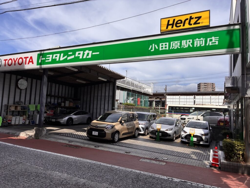 小田原駅西口のロータリー周辺に位置するレンタカー店舗の受付看板と周辺の街並み